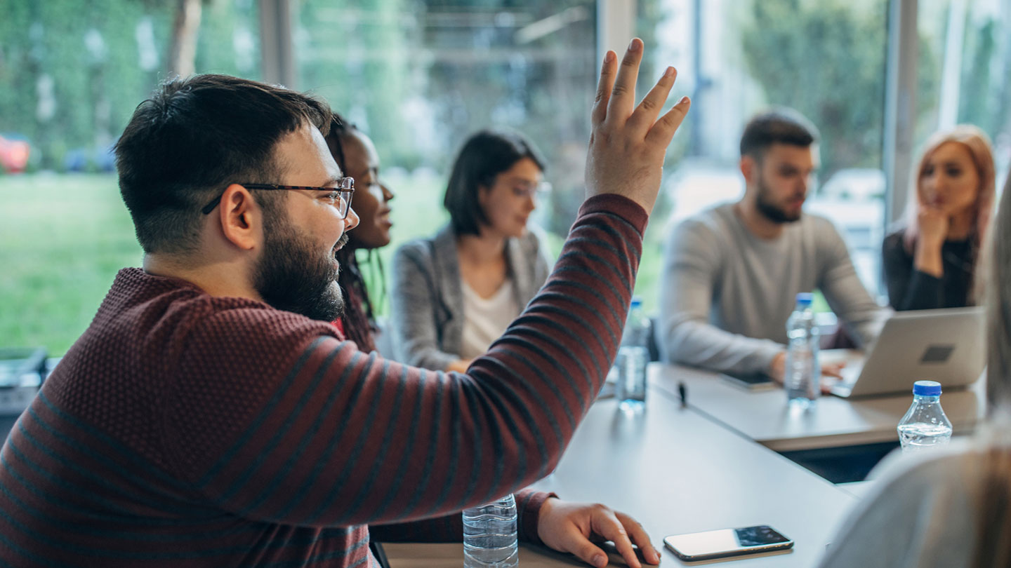 man på möte räcker upp handen