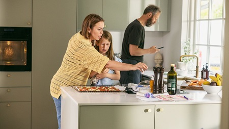 En familj i köket, med en kvinna som serverar, en man som tittar på sin telefon och barn i närheten.