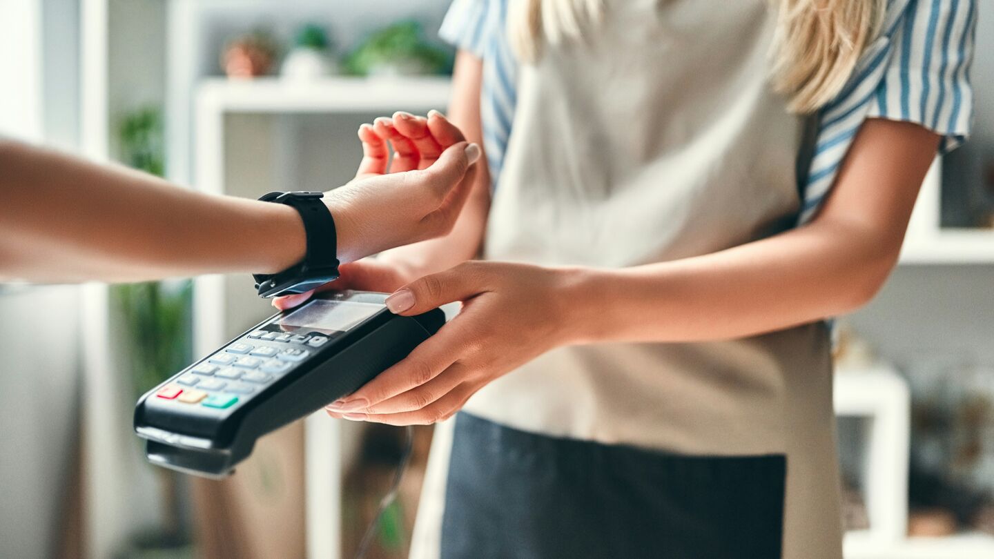 En person genomför en kontaktlös betalning med en smartklocka via en kortterminal.