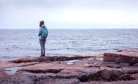 Tjej med ryggsäck står vid havet och blickar ut