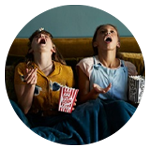 Två personer sitter i en soffa och ser ut att skratta medan de äter popcorn.