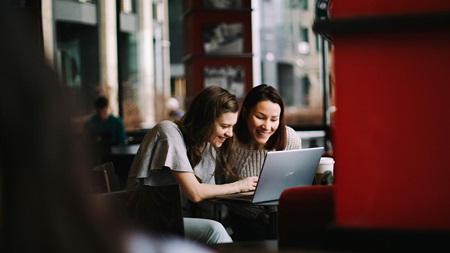 Två personer sitter vid ett bord på ett kafé och tittar på en laptop.