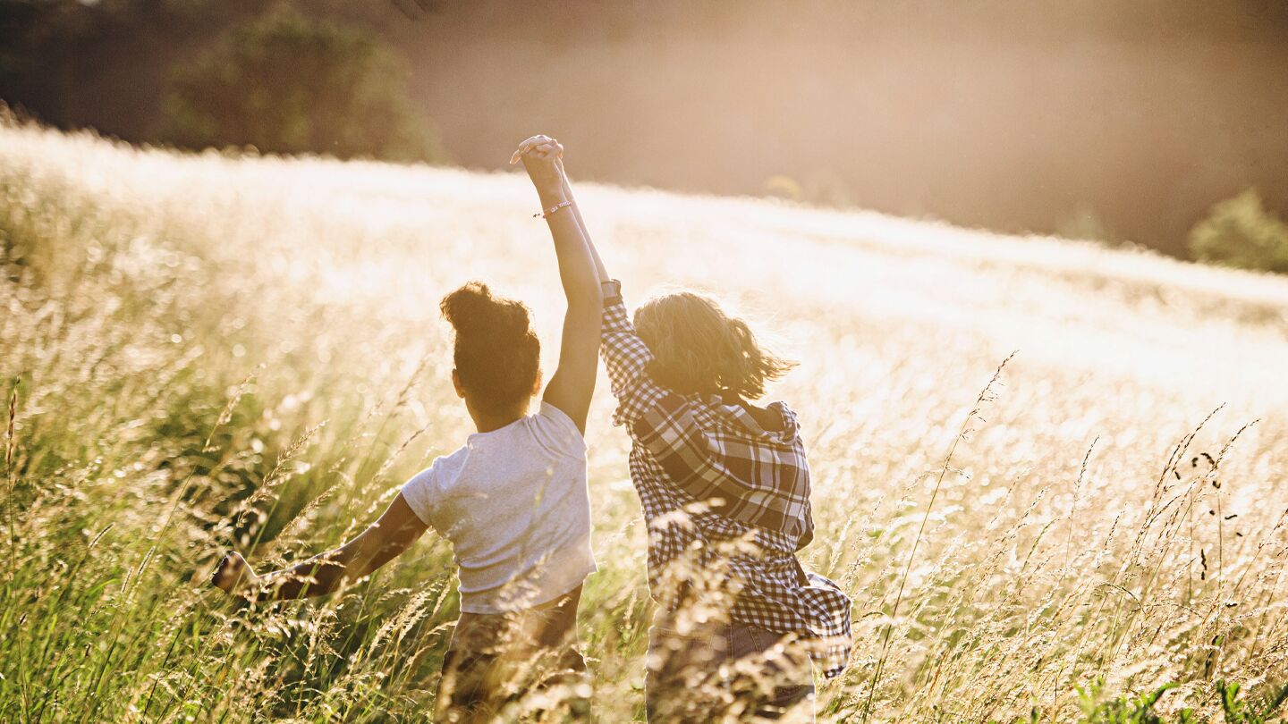 Två personer springer genom en solbelyst äng, hållandes varandra i handen.