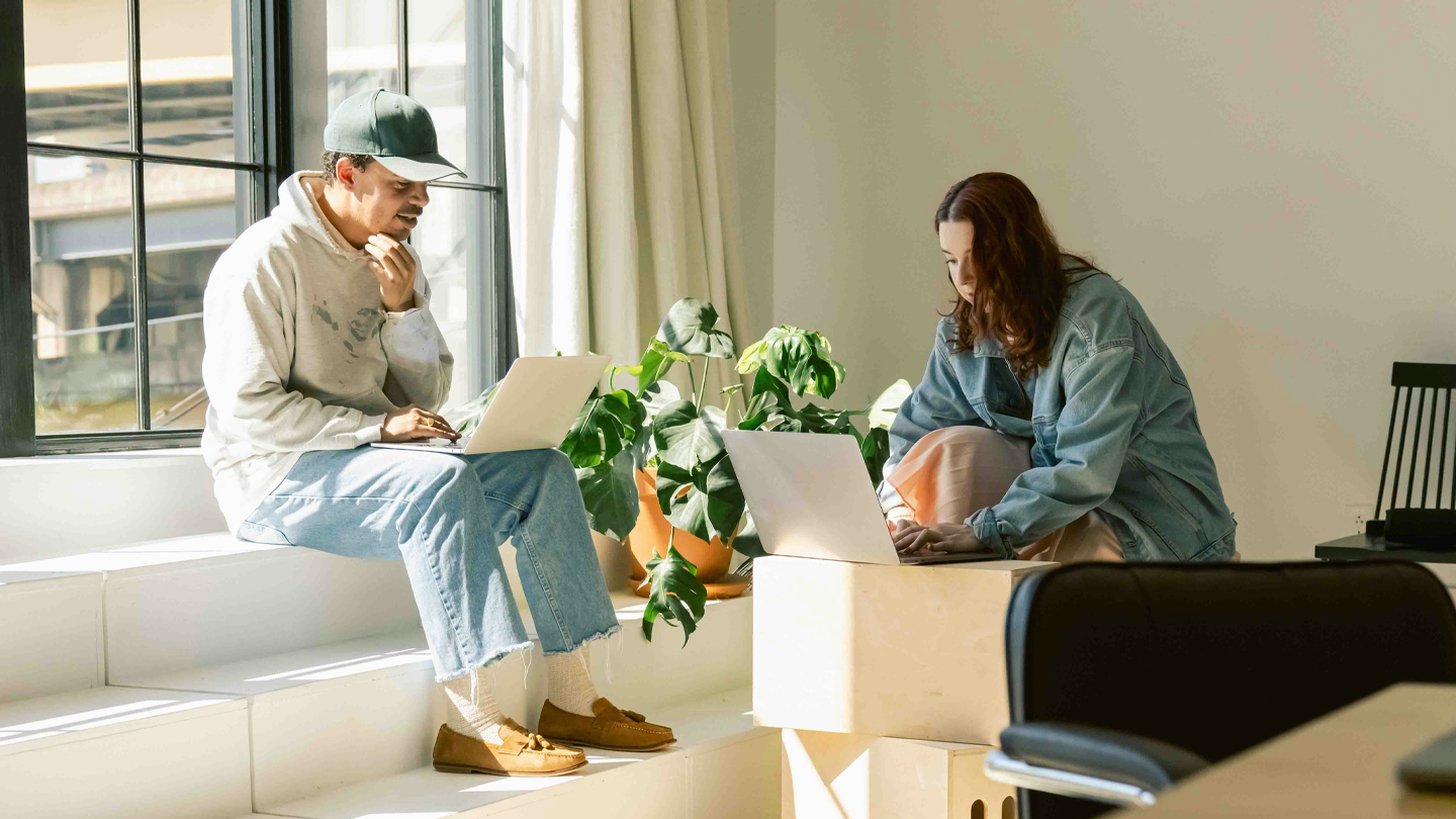 Två personer med laptops i en ljus och modern arbetsmiljö med gröna växter.