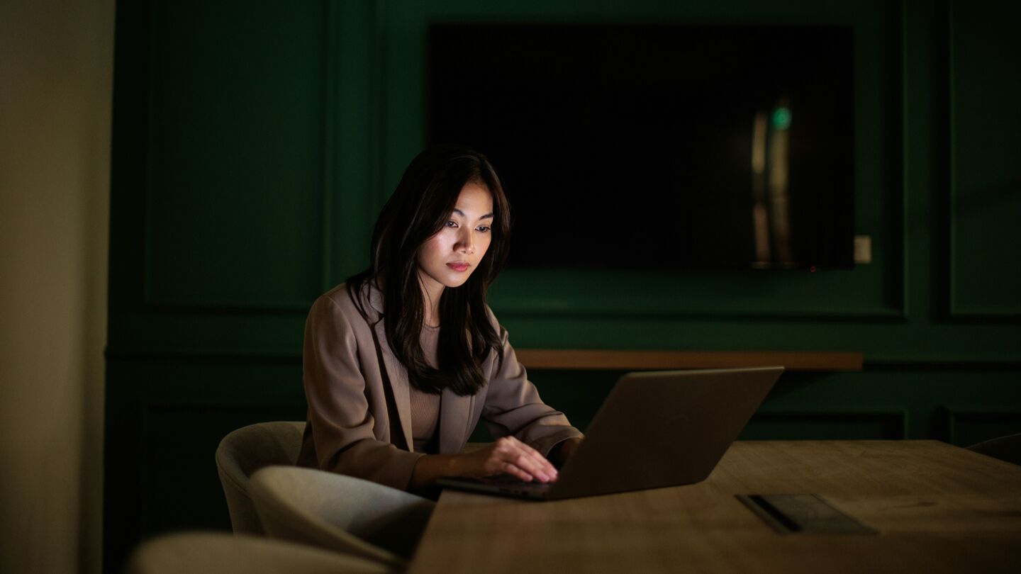 En person sitter vid ett bord och arbetar på en bärbar dator i ett rum med mörkgröna väggar.