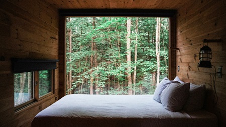 Ett sovrum med träväggar och stora fönster som vetter mot en grönskande skog.