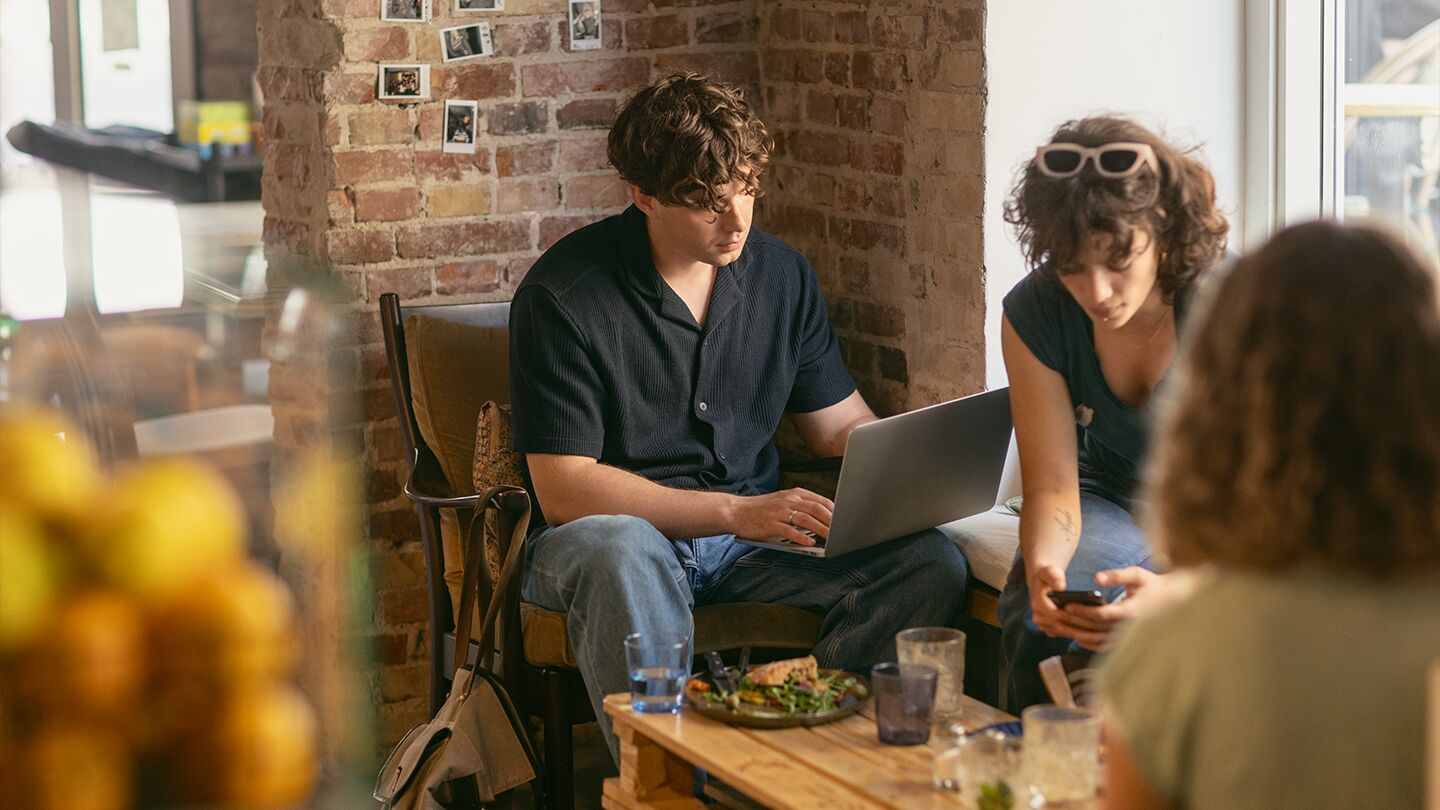 Tre personer sitter på ett café med laptop och mobiltelefon.
