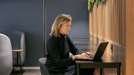 En kvinna sitter vid ett skrivbord och använder en bärbar dator i ett modernt rum med väggpaneler i trä.