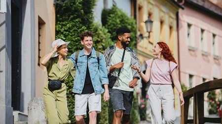 Fyra unga vuxna promenerar tillsammans på en solig stadsgata med färgglada hus i bakgrunden.