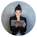 En person står avslappnat mot en betongvägg i ett modernt kontorsutrymme och arbetar på en surfplatta. 