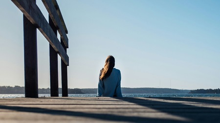 Person står ensam på en kulle i ett öppet landskap med molnig himmel