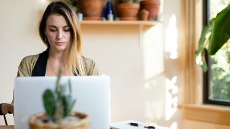 Person som arbetar hemifrån med en bärbar dator, antecknar och pratar i telefon.