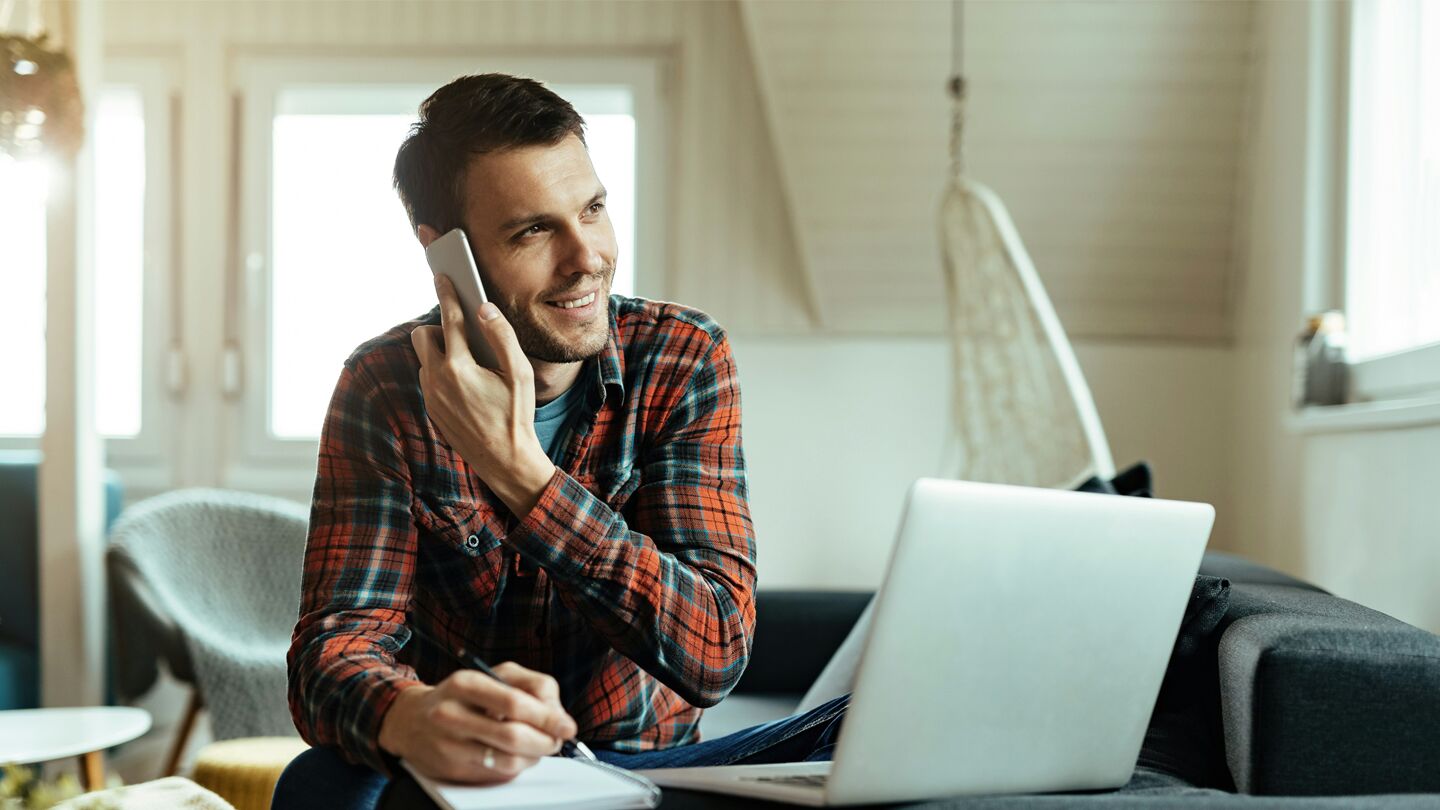 Person som arbetar hemifrån med en bärbar dator, antecknar och pratar i telefon.