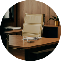 Ett kontor med ett skrivbord, en beige stol, papper och en penna. En orkidé står på en hylla i bakgrunden.