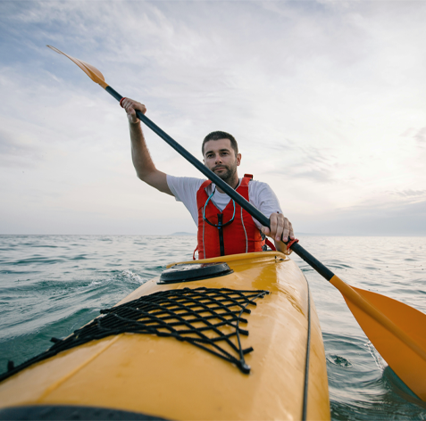 Person paddlar en gul kajak på öppet vatten under en ljus himmel.