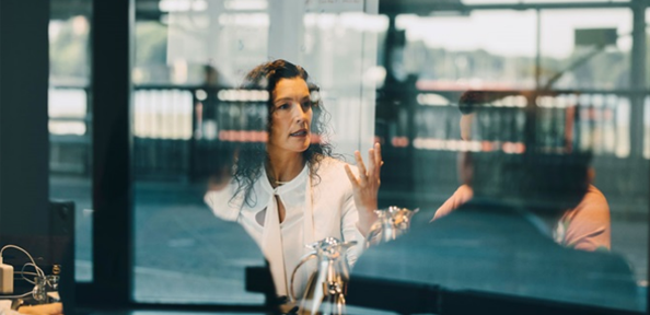 Person i samtal vid ett bord, reflektioner syns i glaset.