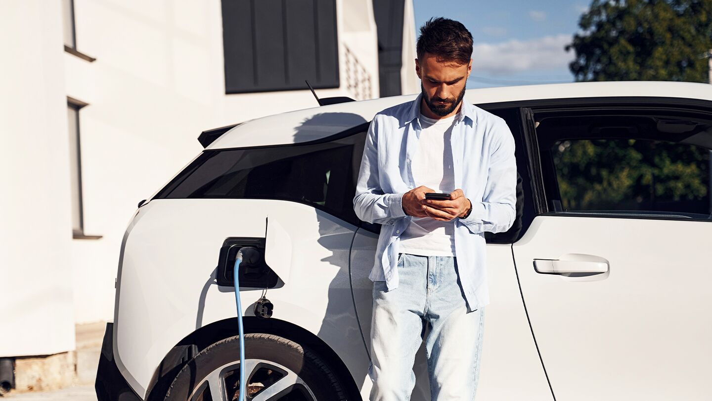 Person står vid en elbil som laddas utanför ett modernt hus.