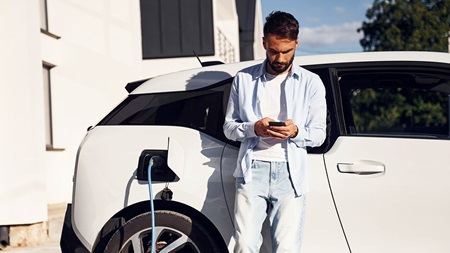 Person står vid en elbil som laddas utanför ett modernt hus.