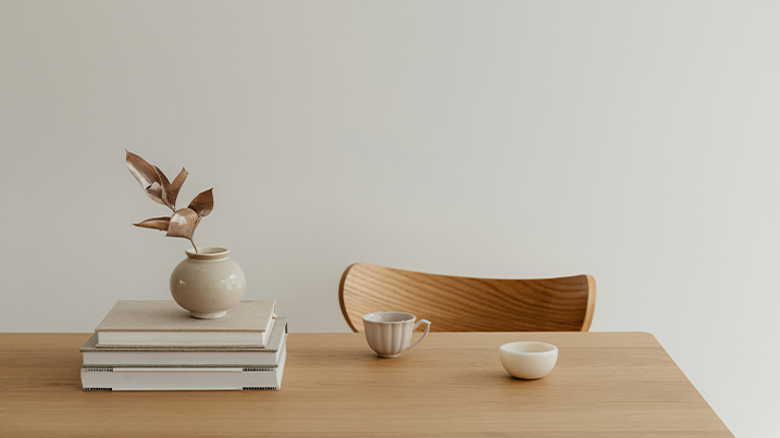 En minimalistisk träbord med en stapel böcker, en liten vas med dekorativa blad.