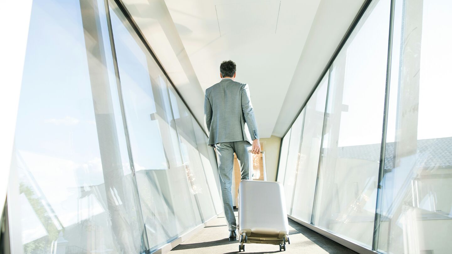 Man i kostym går med resväska i en ljus korridor.