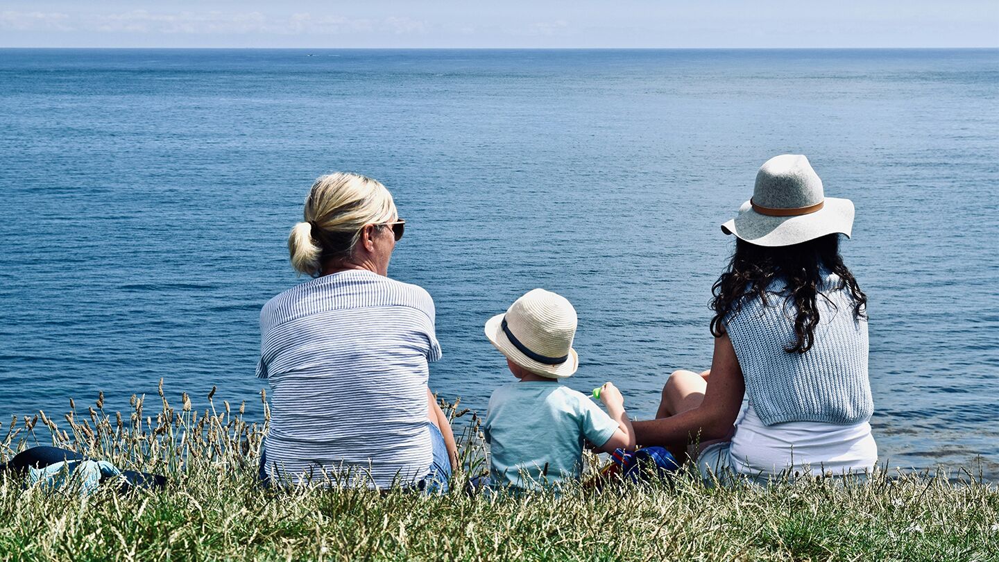 Tre personer sitter på en klippa vid havet och ser ut över vattnet.