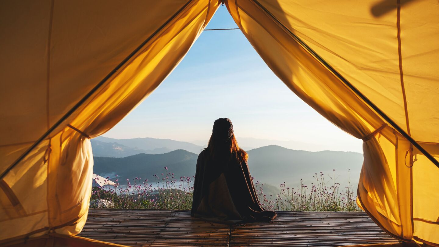 Person sitter i tält och ser ut över berg och landskap.