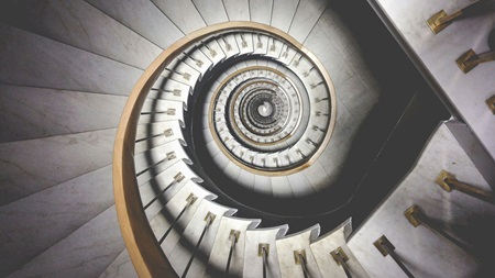 Spiralformad trappa i marmor med gyllene detaljer, sedd uppifrån.