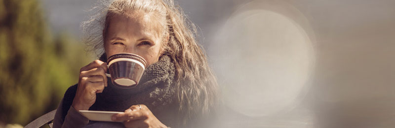 Kvinna sitter med kaffekopp och tittar på mobil