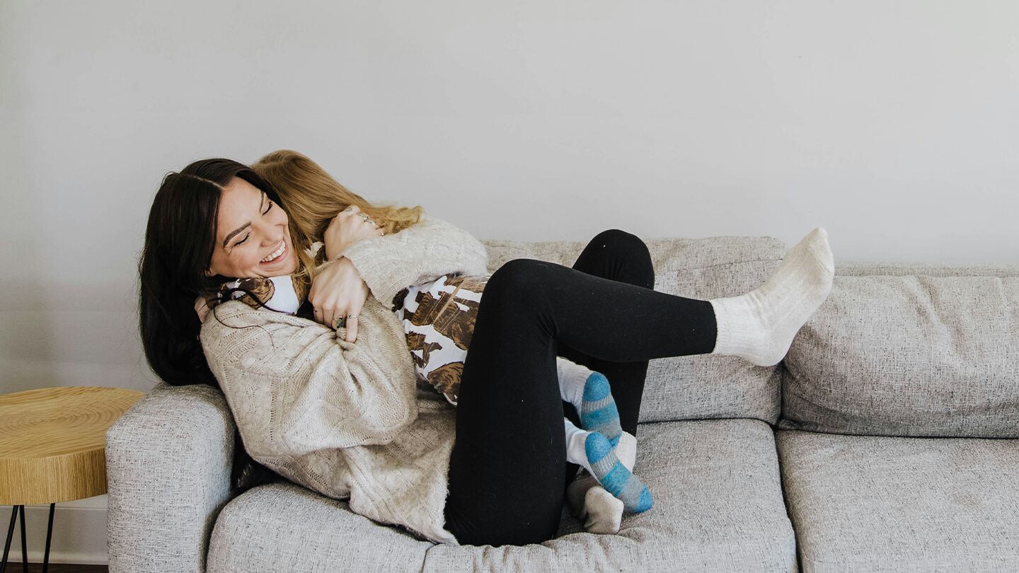 En person som sitter i en soffa och håller ett barn i en avslappnad hemmamiljö.