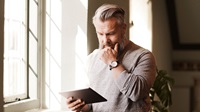 Man funderar över sitt sparkapital och kikar på sin Ipad vid ett fönster.