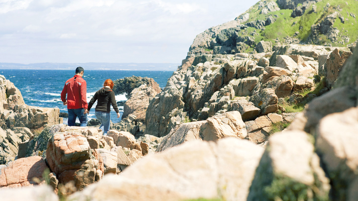 två personer går bland stenar vid vatten